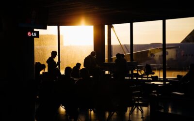 Travelers sitting in an airport terminal at sunset, silhouetted against the backdrop of an airplane.