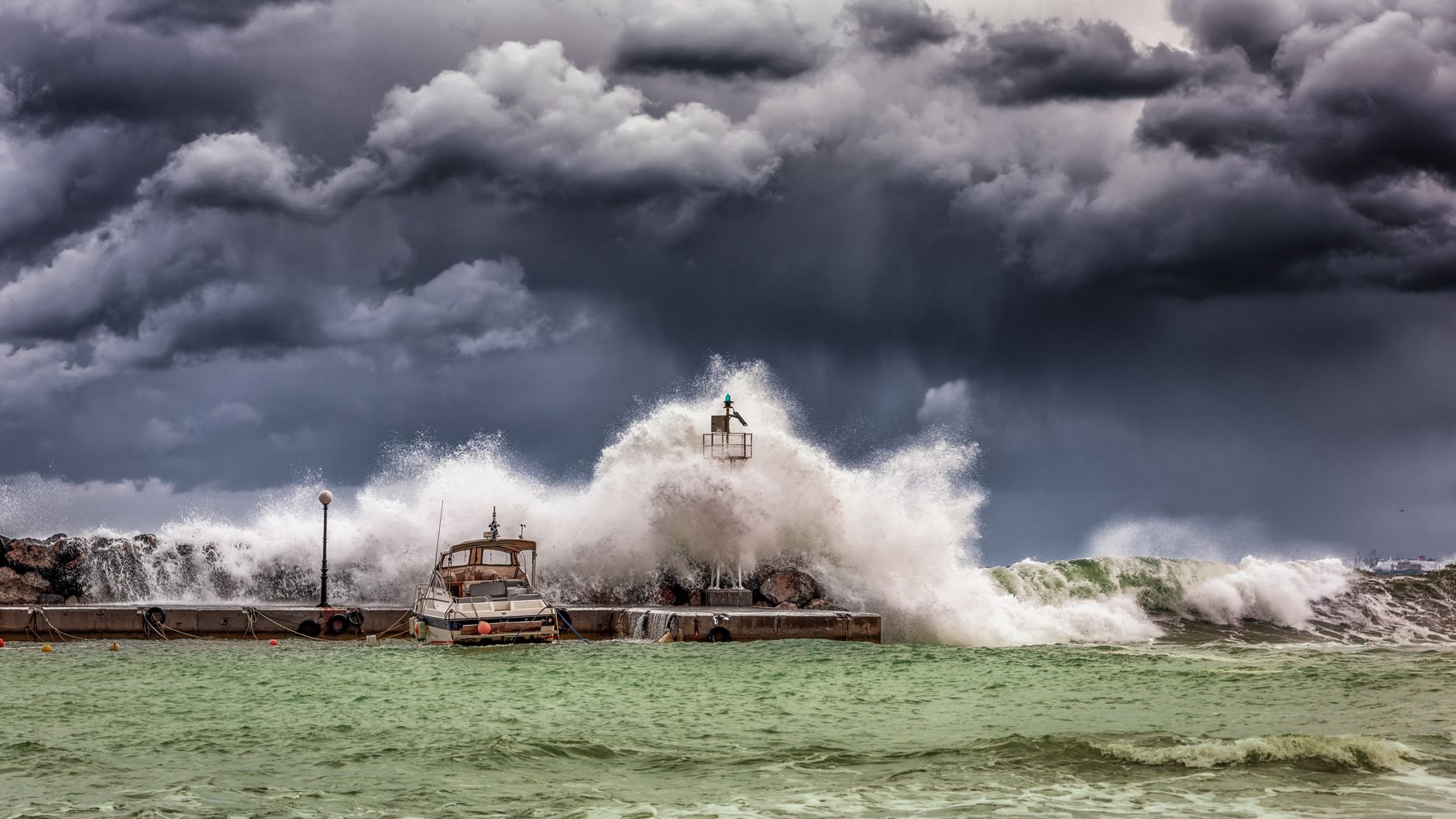 Powerful storm waves crashing against a coastal pier and lighthouse under dark skies