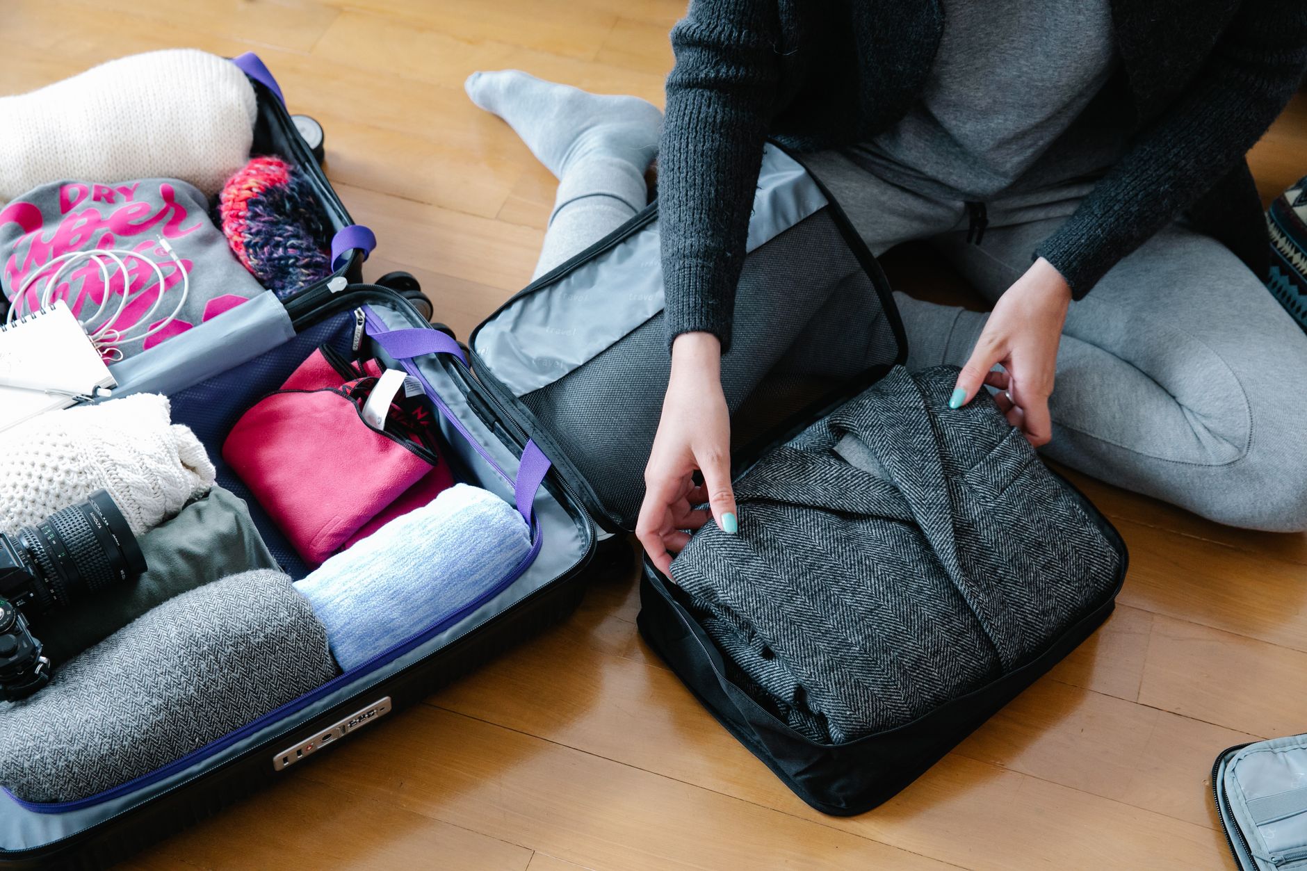 Traveller organising folded clothing and camera gear in a suitcase for a shoulder-season trip