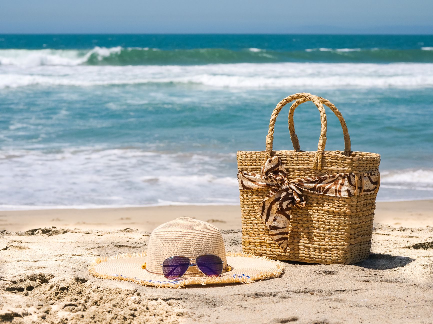 Straw sun hat, beach bag and sunglasses on sand ready for a hot US summer trip