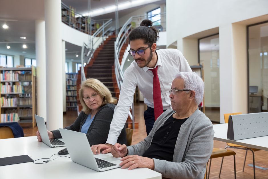 Adult child helping an elderly parent complete an online travel form on a laptop